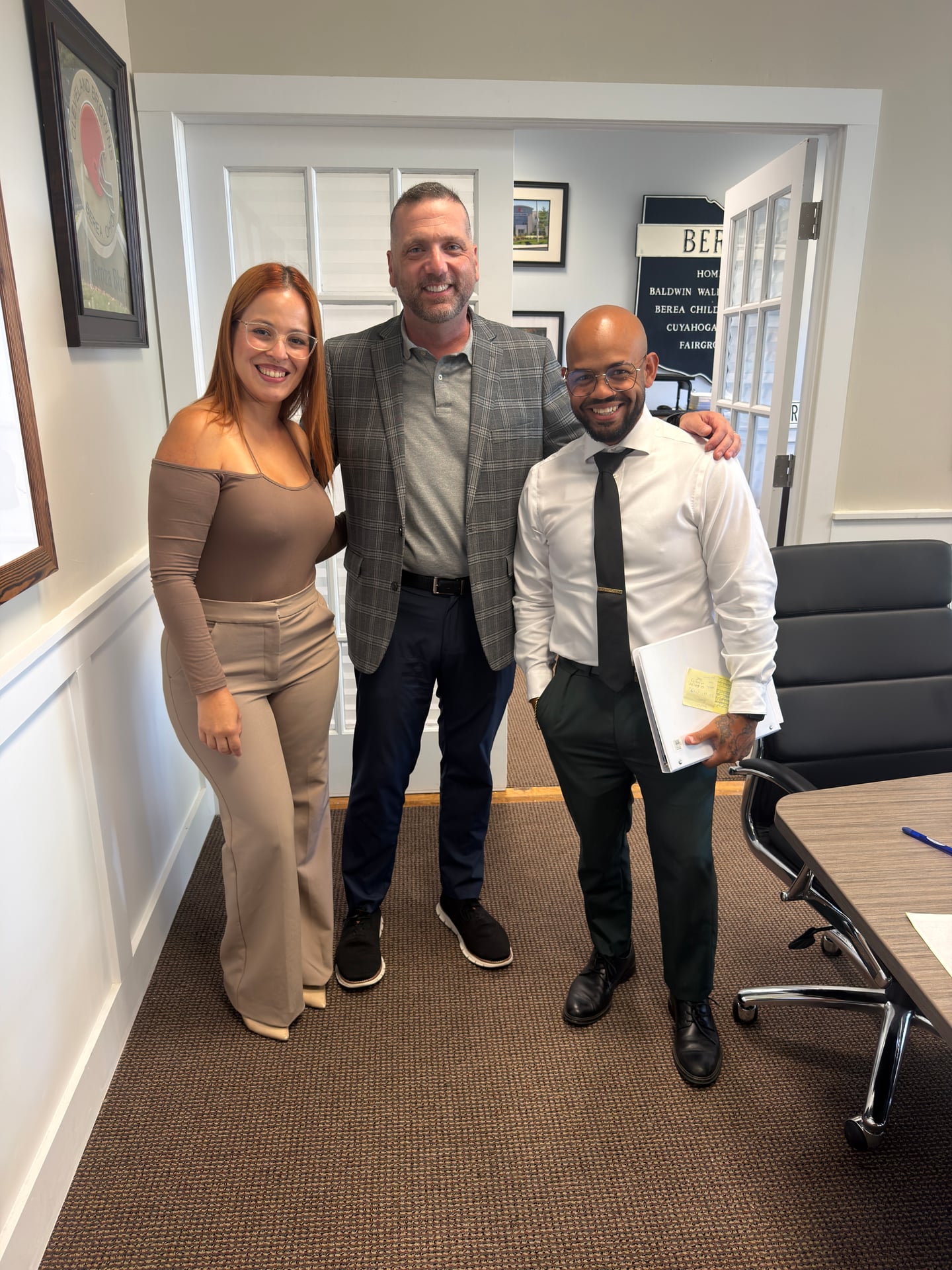 Three people smiling together in an office, with one person holding a binder.