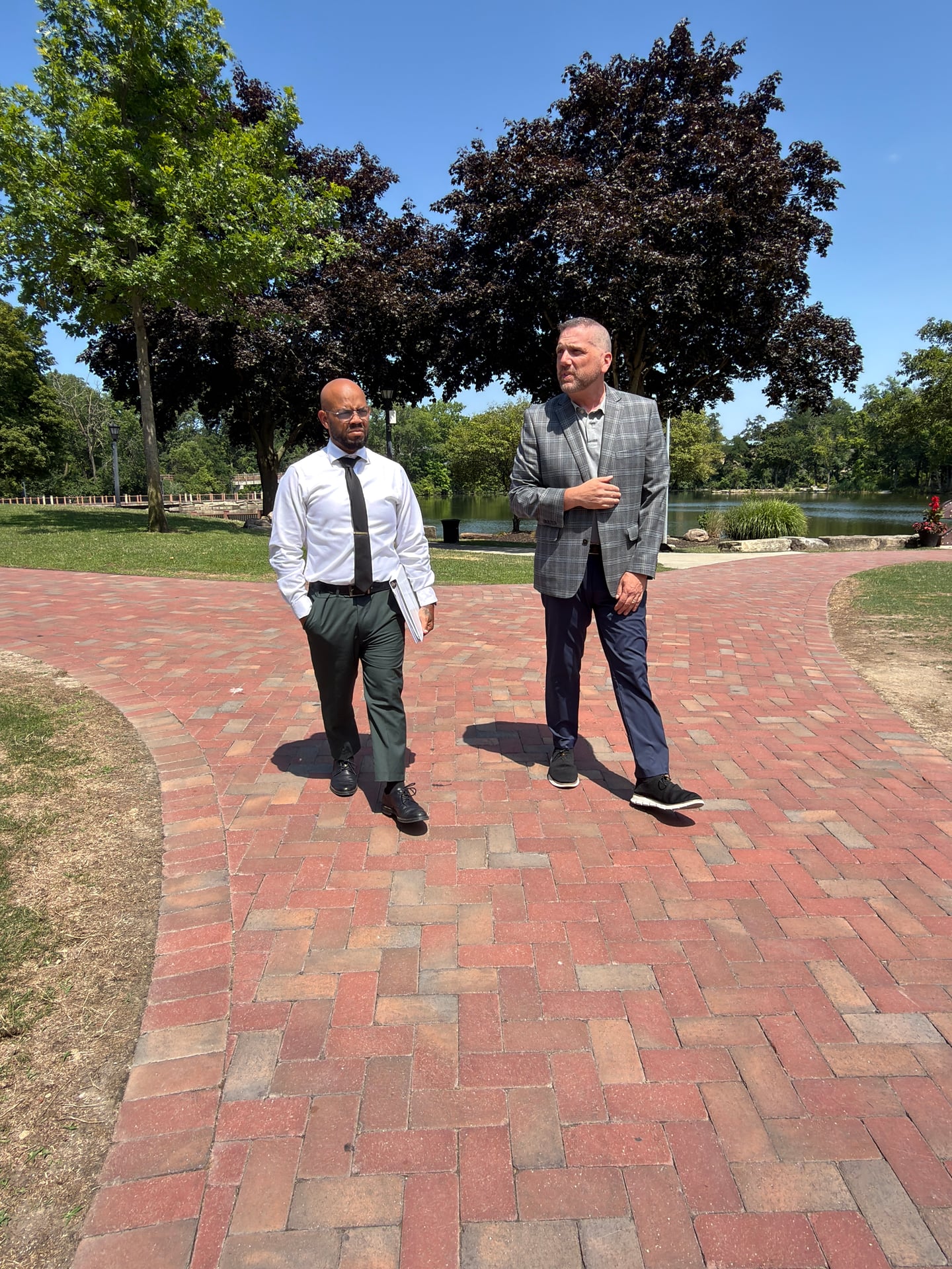 Two people standing on a brick path beside a pond and trees.
