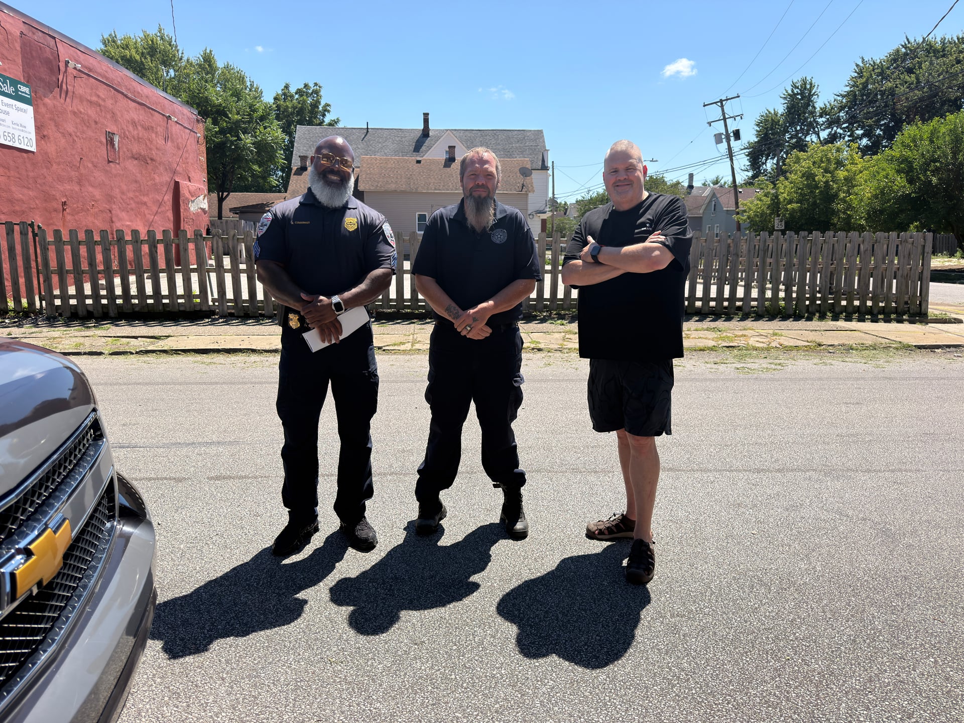Three people posing together on a neighborhood street.