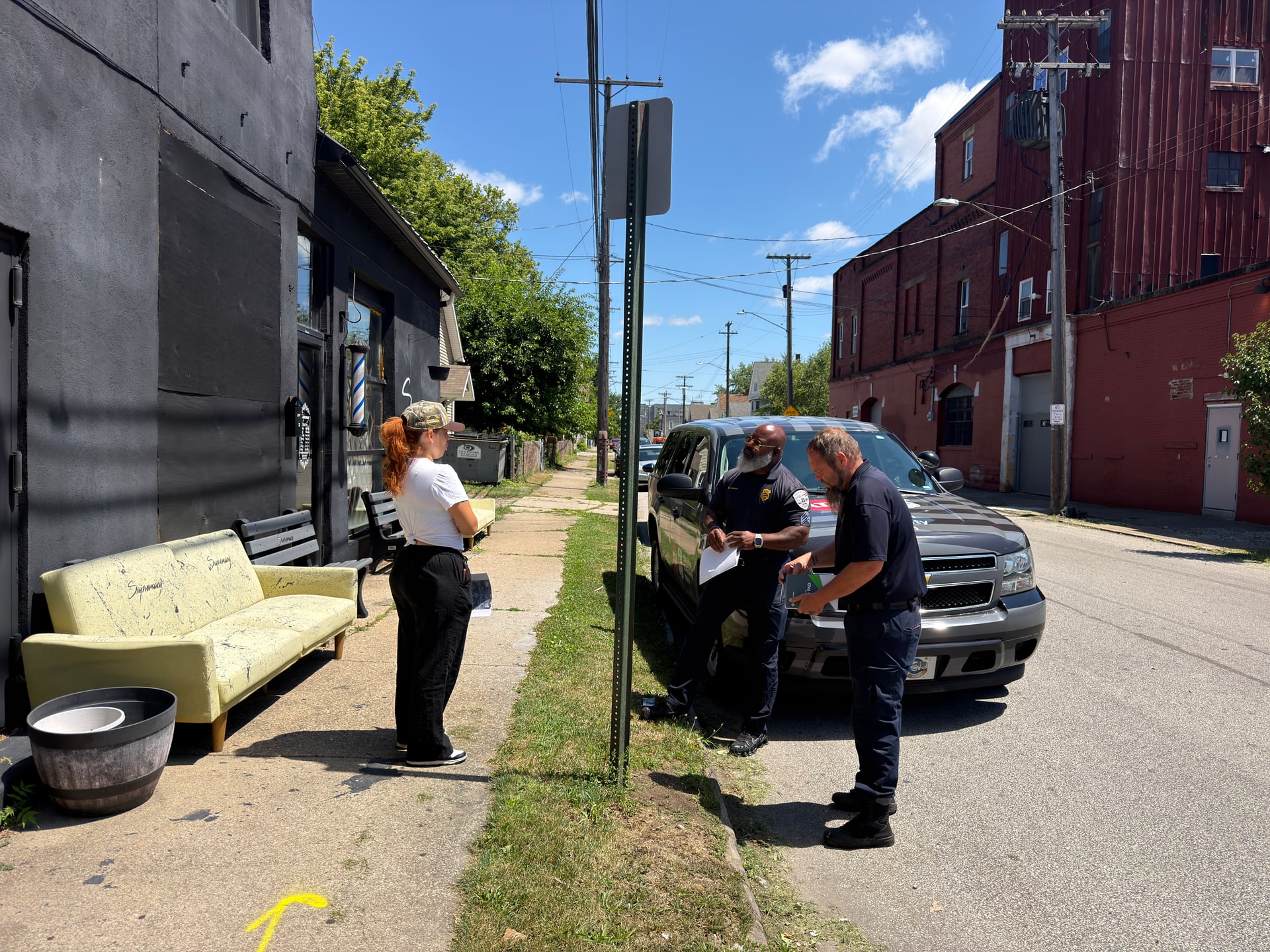 Three people with papers gathered beside a vehicle outside a storefront.