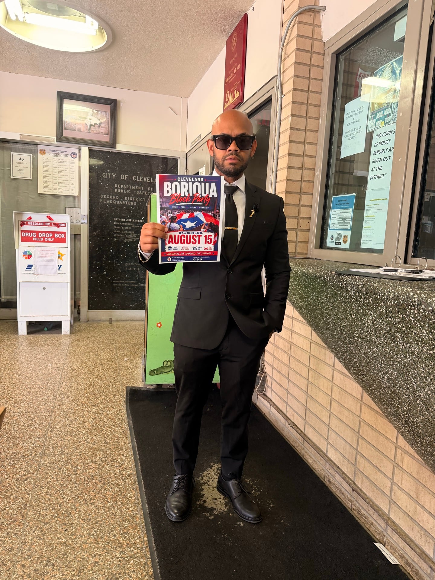 A person in a suit holding an early August 15 block party flyer in a public-safety building lobby.