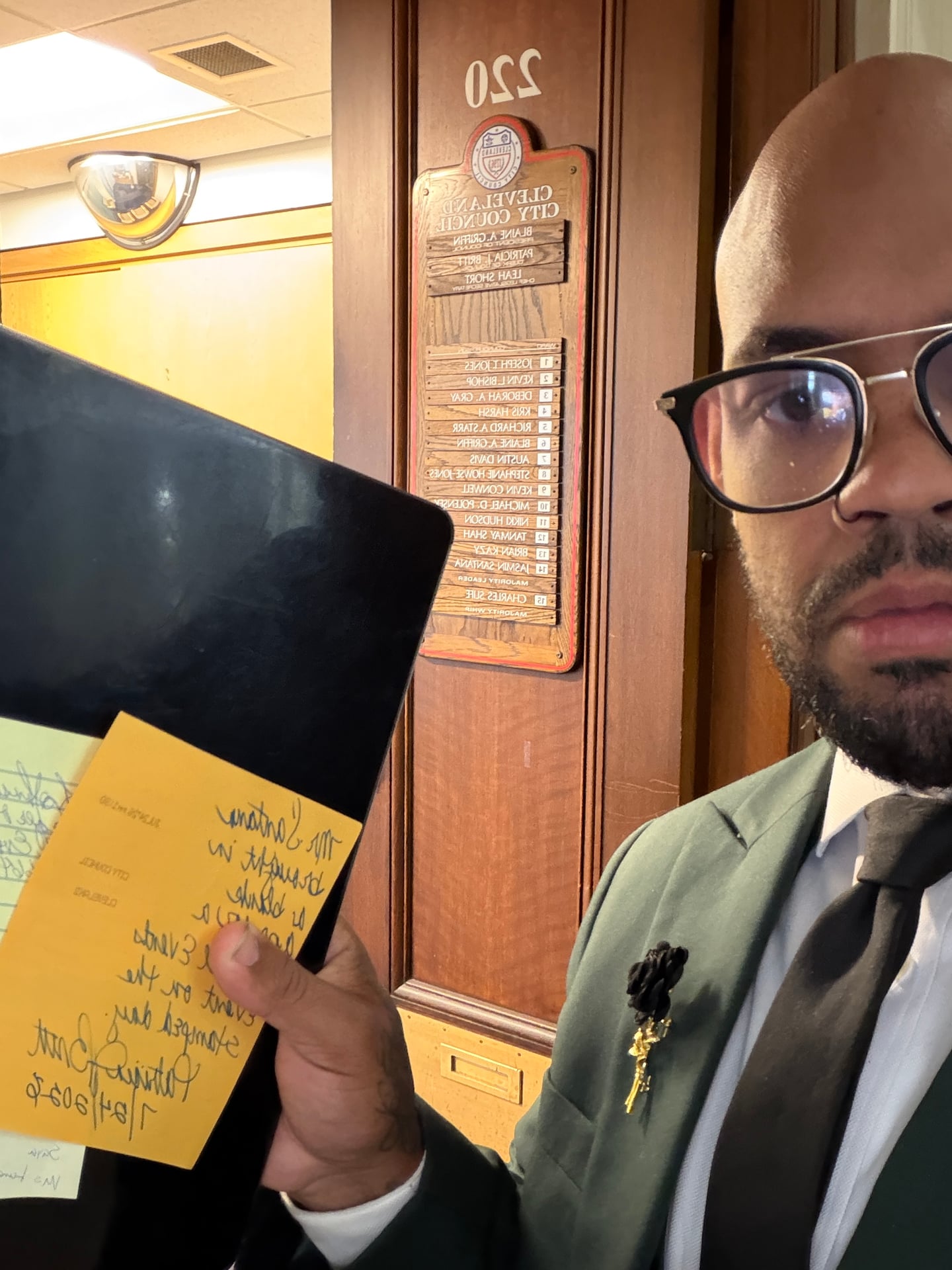 A person holding a binder with handwritten notes beside a Cleveland City Council office sign.
