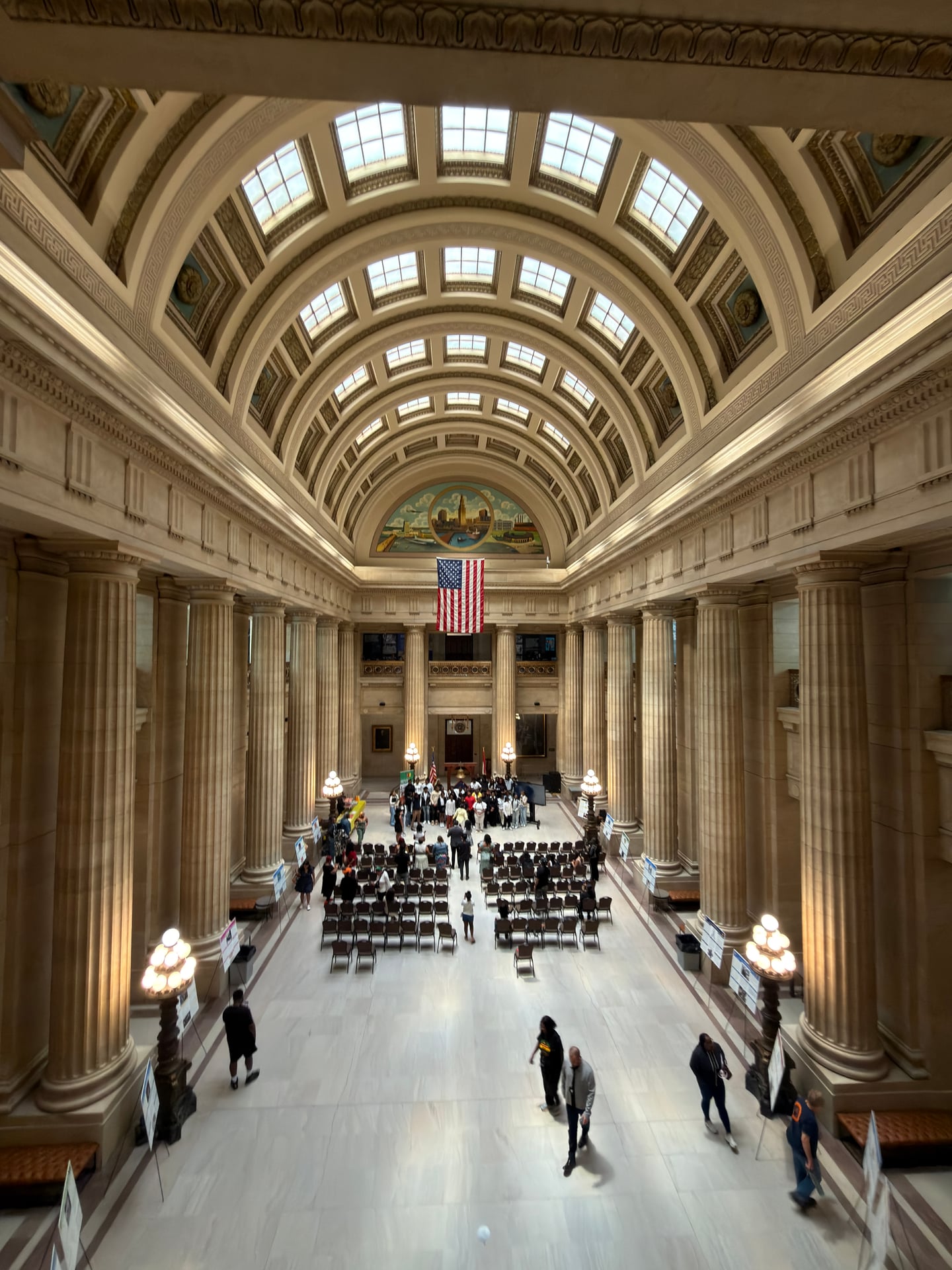 A view down a large stone hall with an arched ceiling, columns, rows of chairs, and people gathered below.