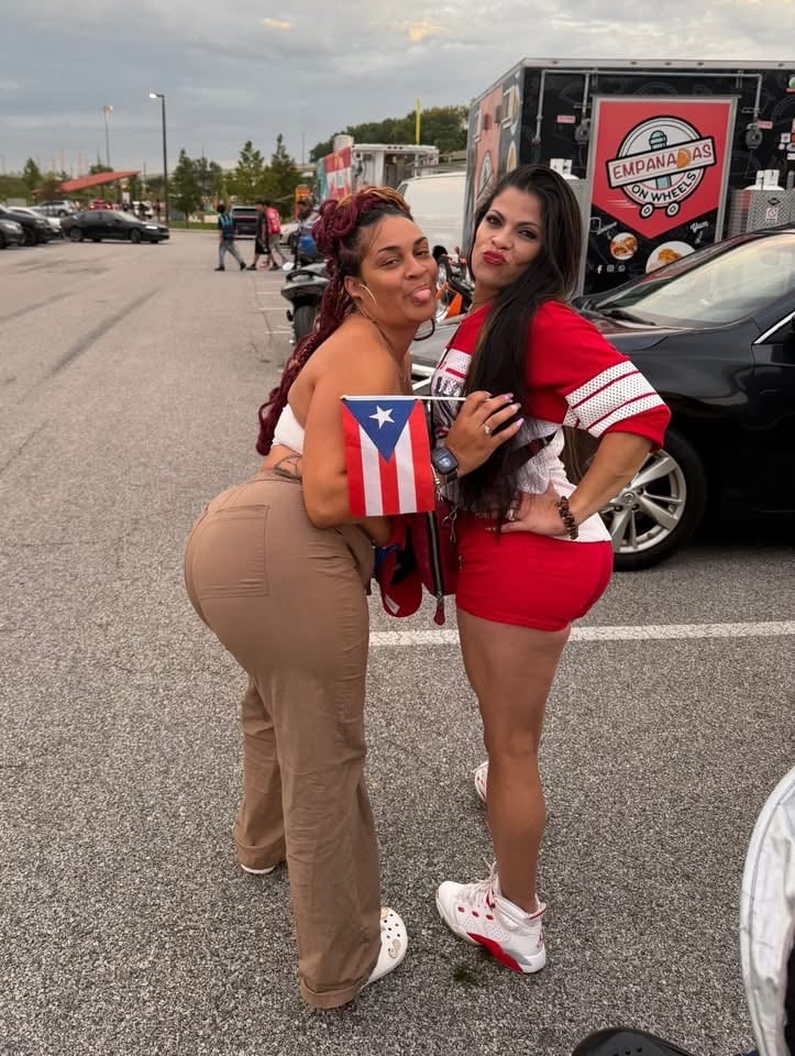 Two people posing with a Puerto Rican flag near the Empanadas on Wheels food truck.