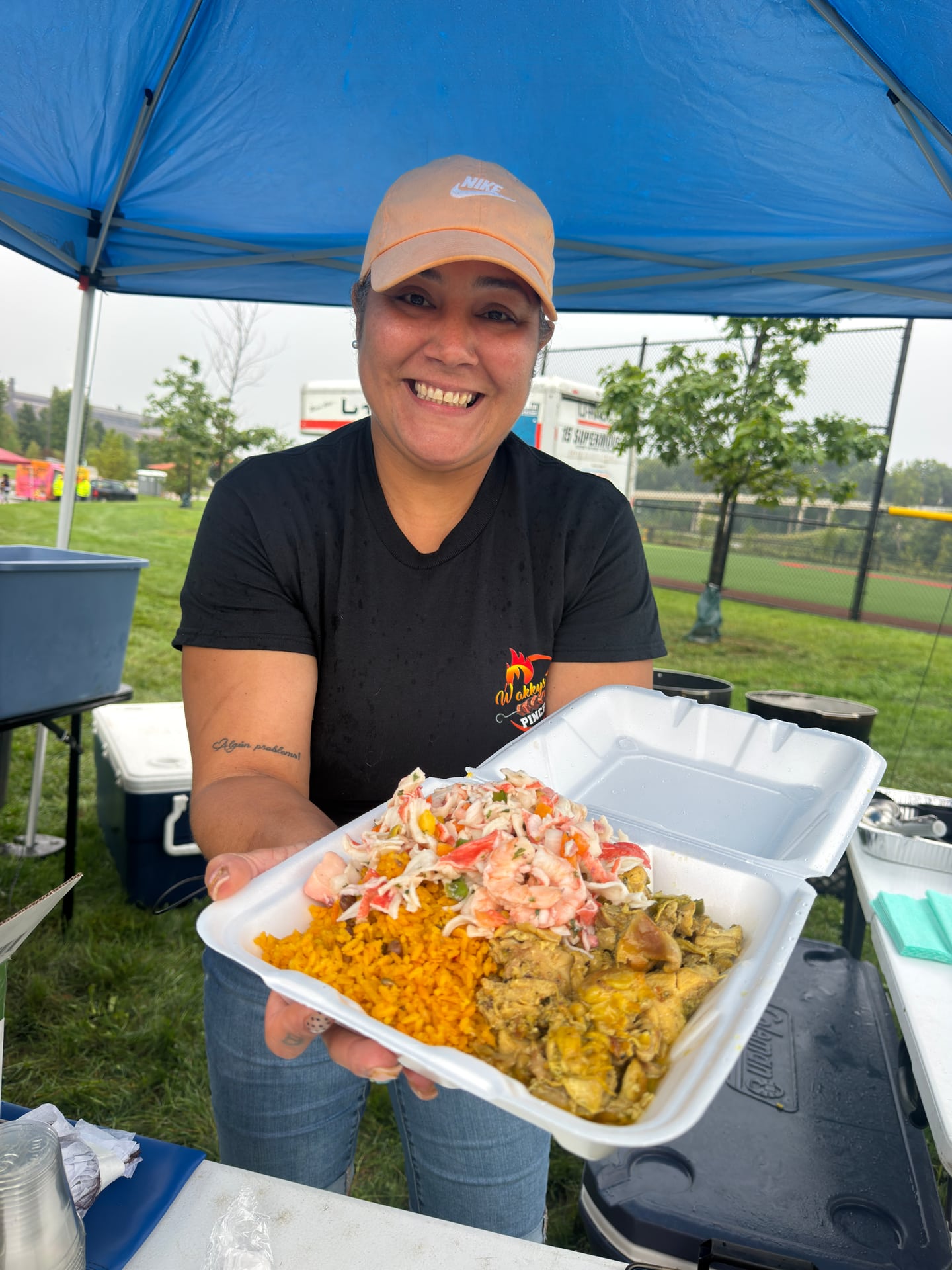 A smiling food vendor holding an open takeout container filled with rice and other dishes.