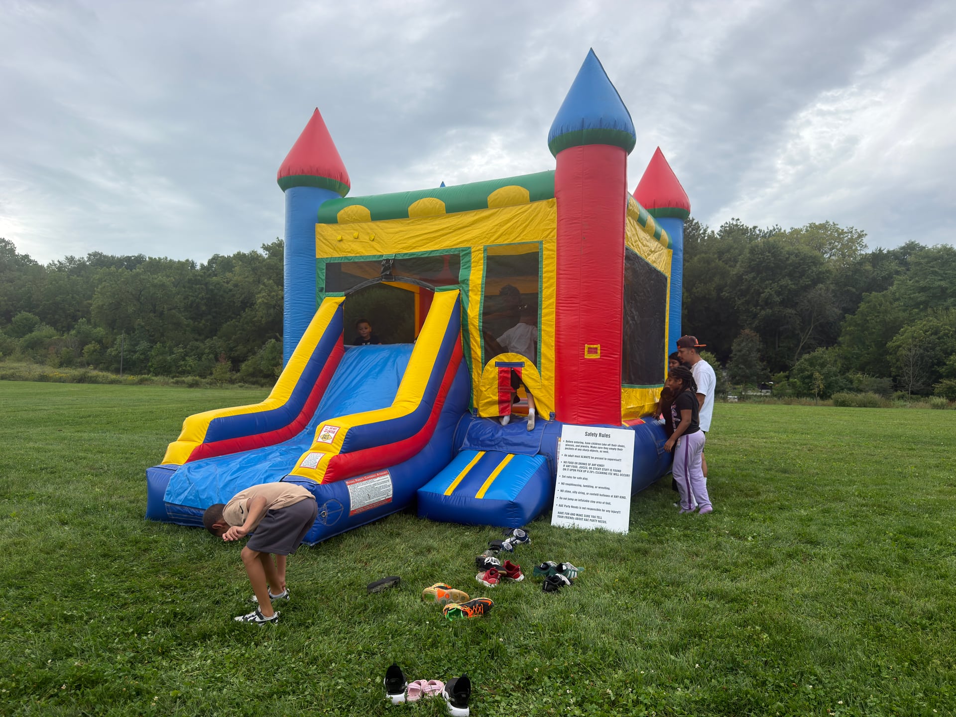 Children beside and inside a colorful inflatable bounce house and slide on the field.