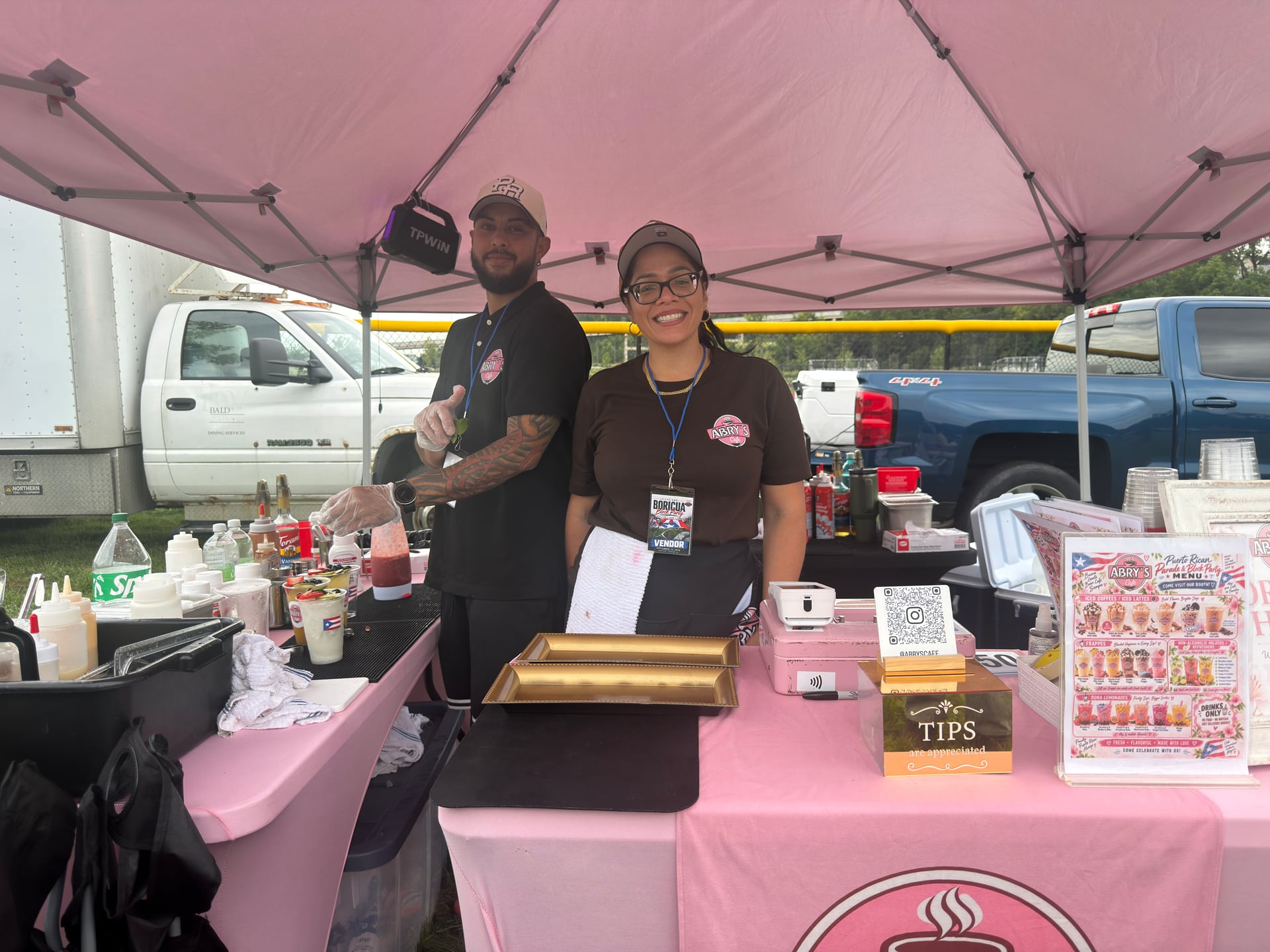Two people behind an Abry’s Café vendor table displaying drinks and a menu.