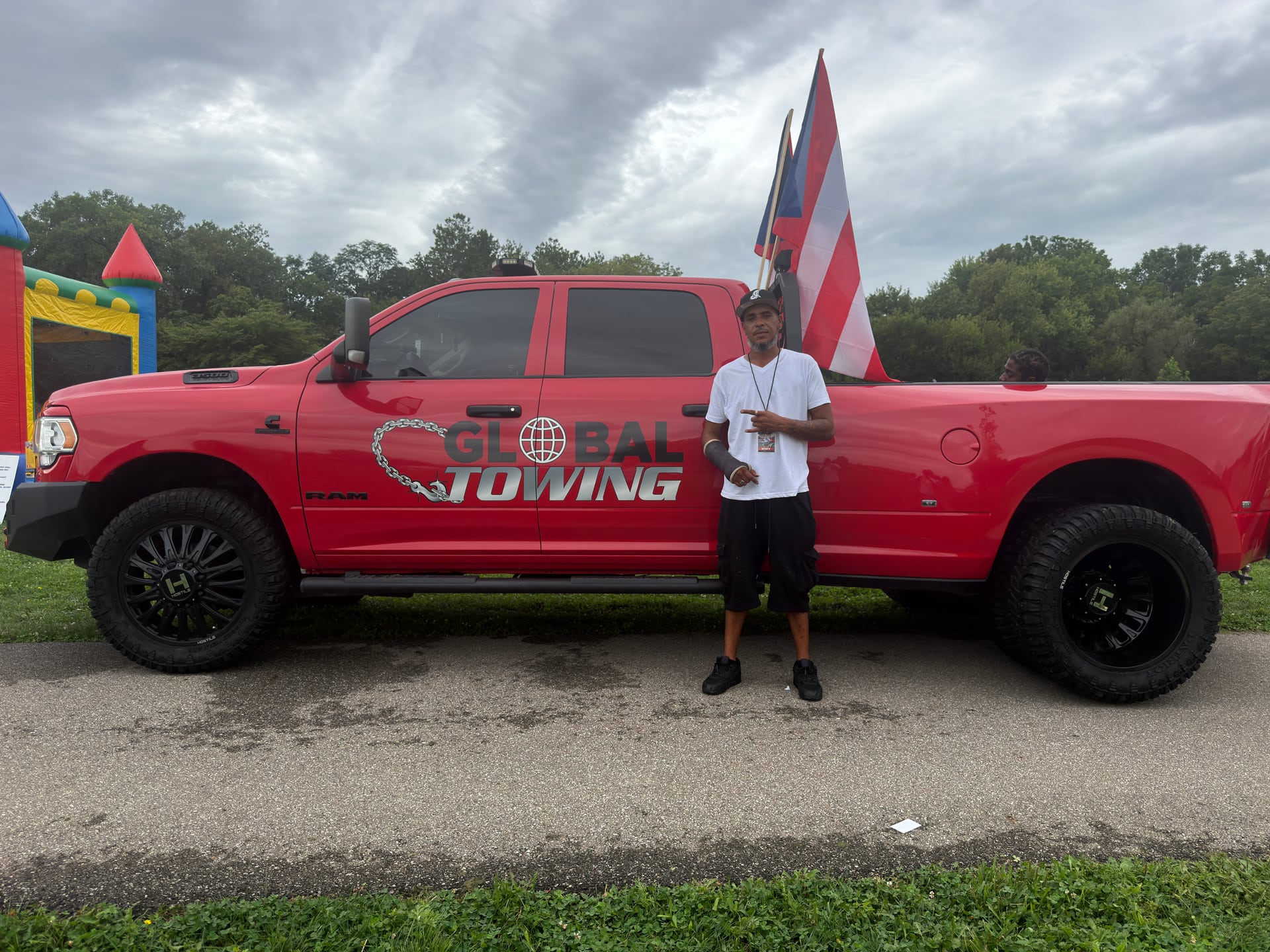 A person posing beside a red Global Towing pickup truck carrying flags.