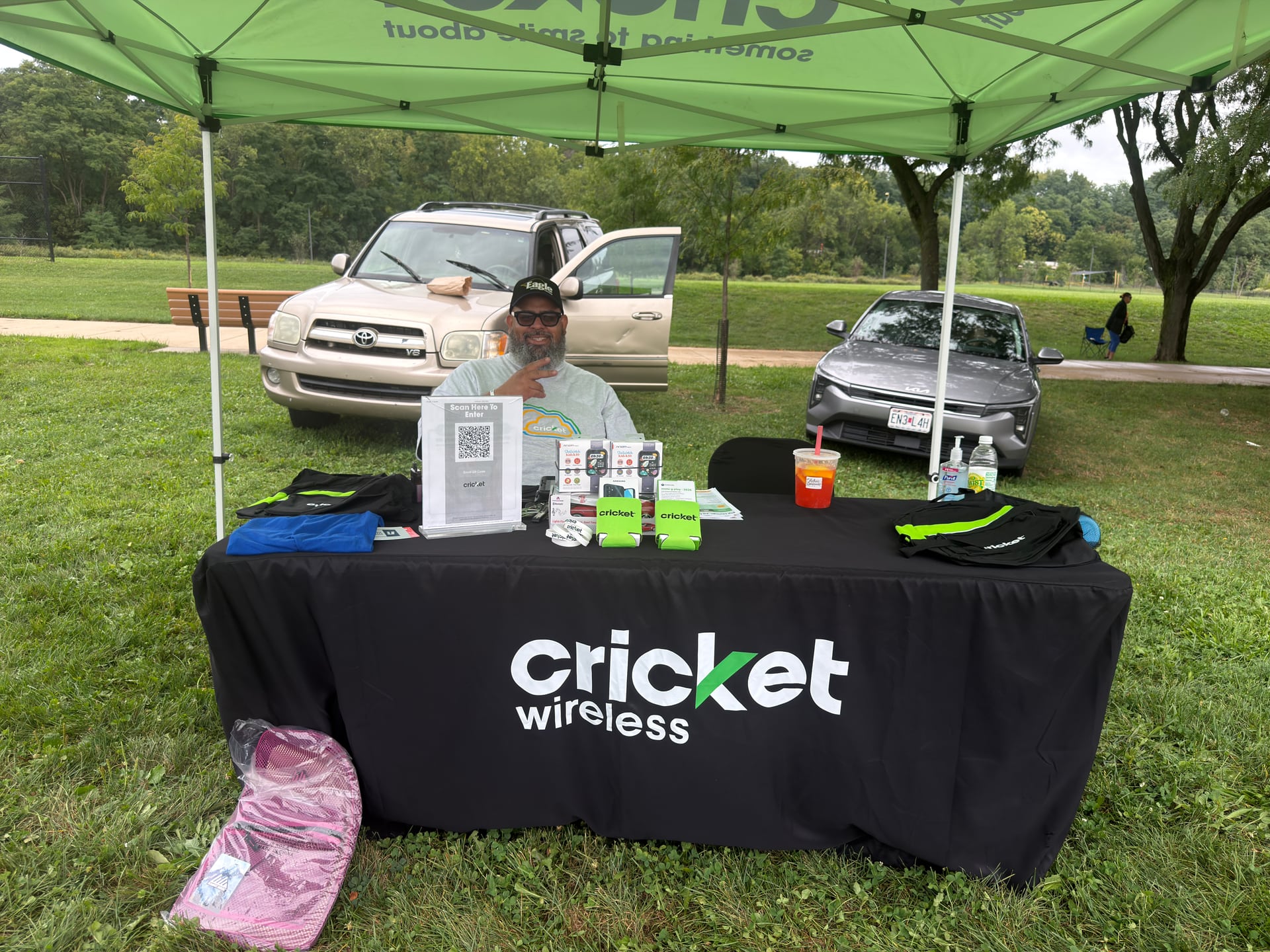 A person behind a Cricket Wireless display table beneath a green canopy.