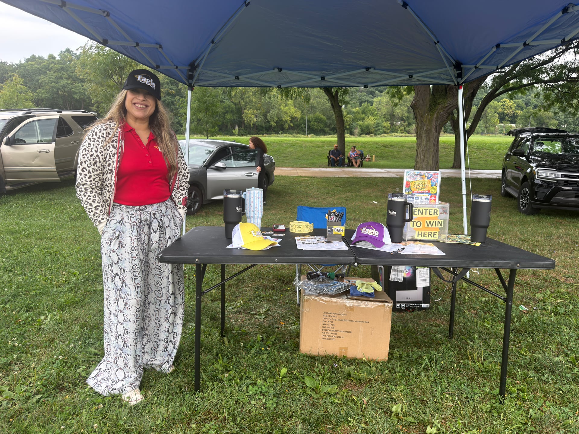 A smiling person beside an Eagle-branded display of hats, cups, and promotional materials.