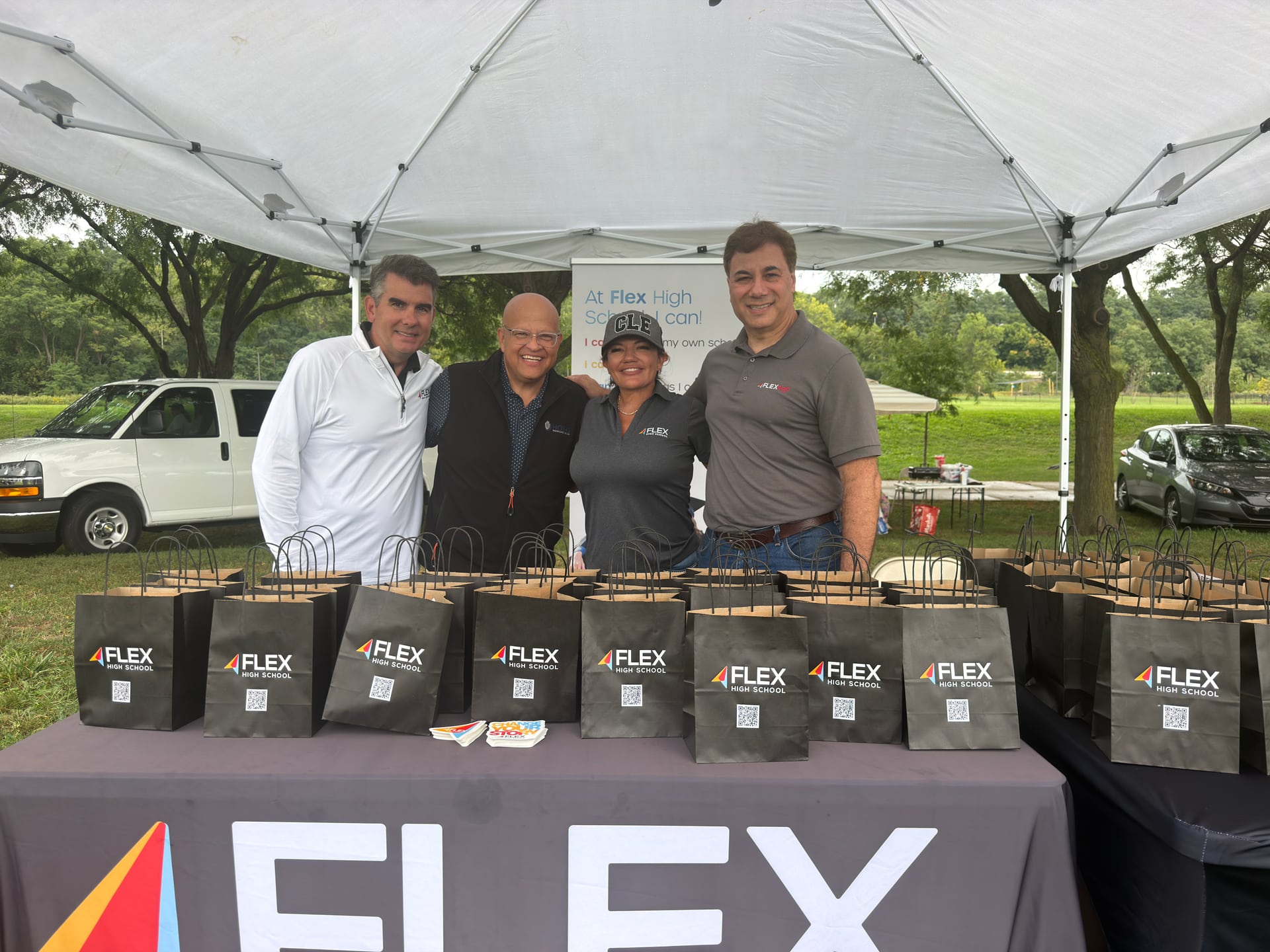 Four people behind a Flex High School table covered with branded giveaway bags.