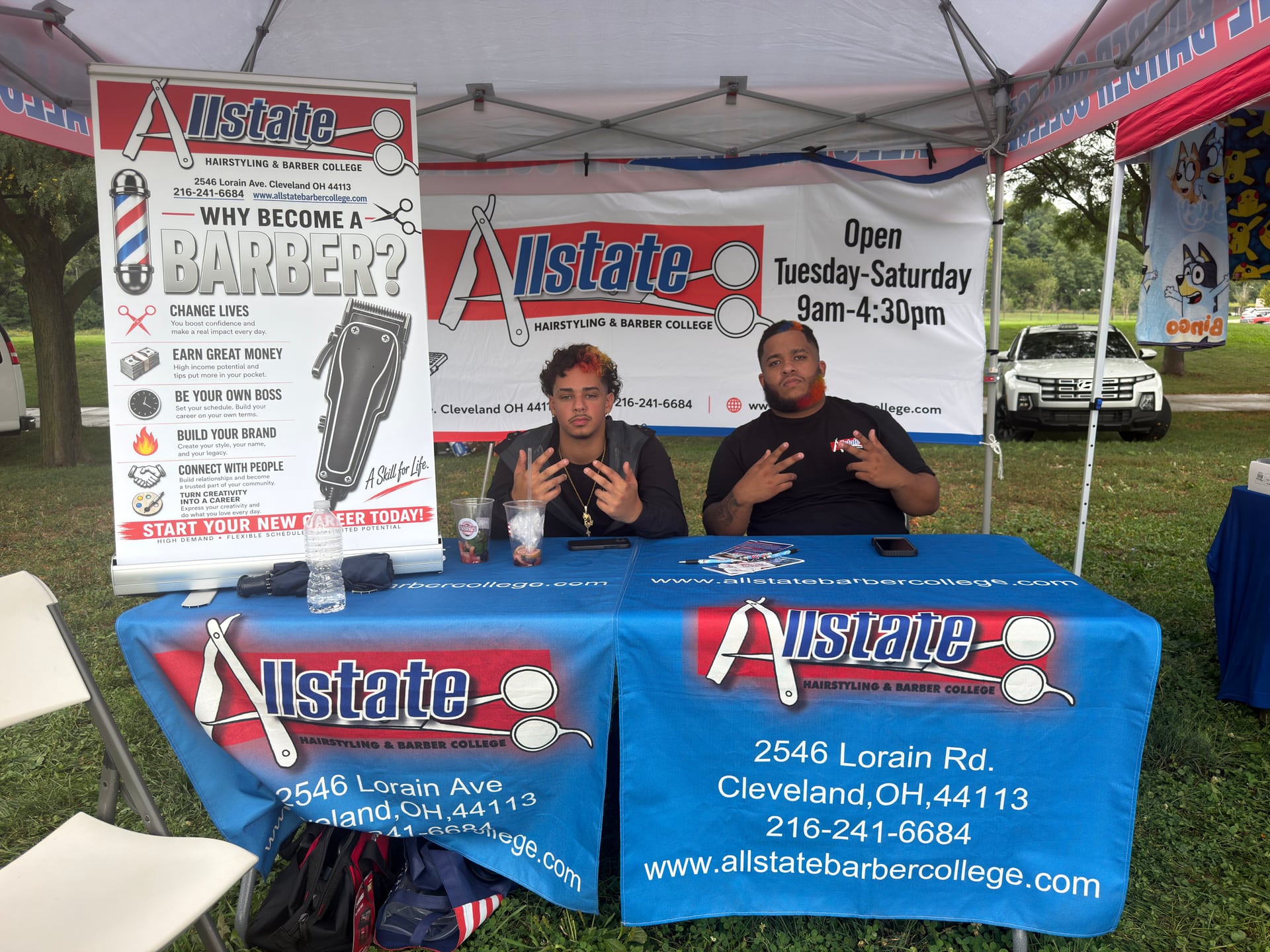 Two people behind an Allstate Hairstyling and Barber College information table.