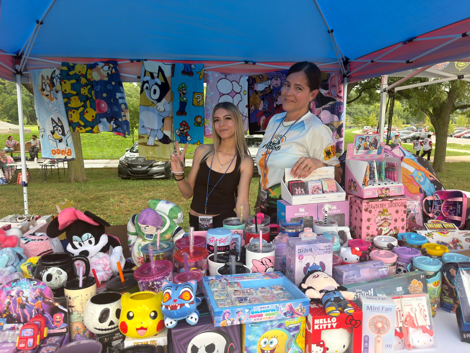 Two people at a vendor table filled with colorful cups, toys, and character merchandise.