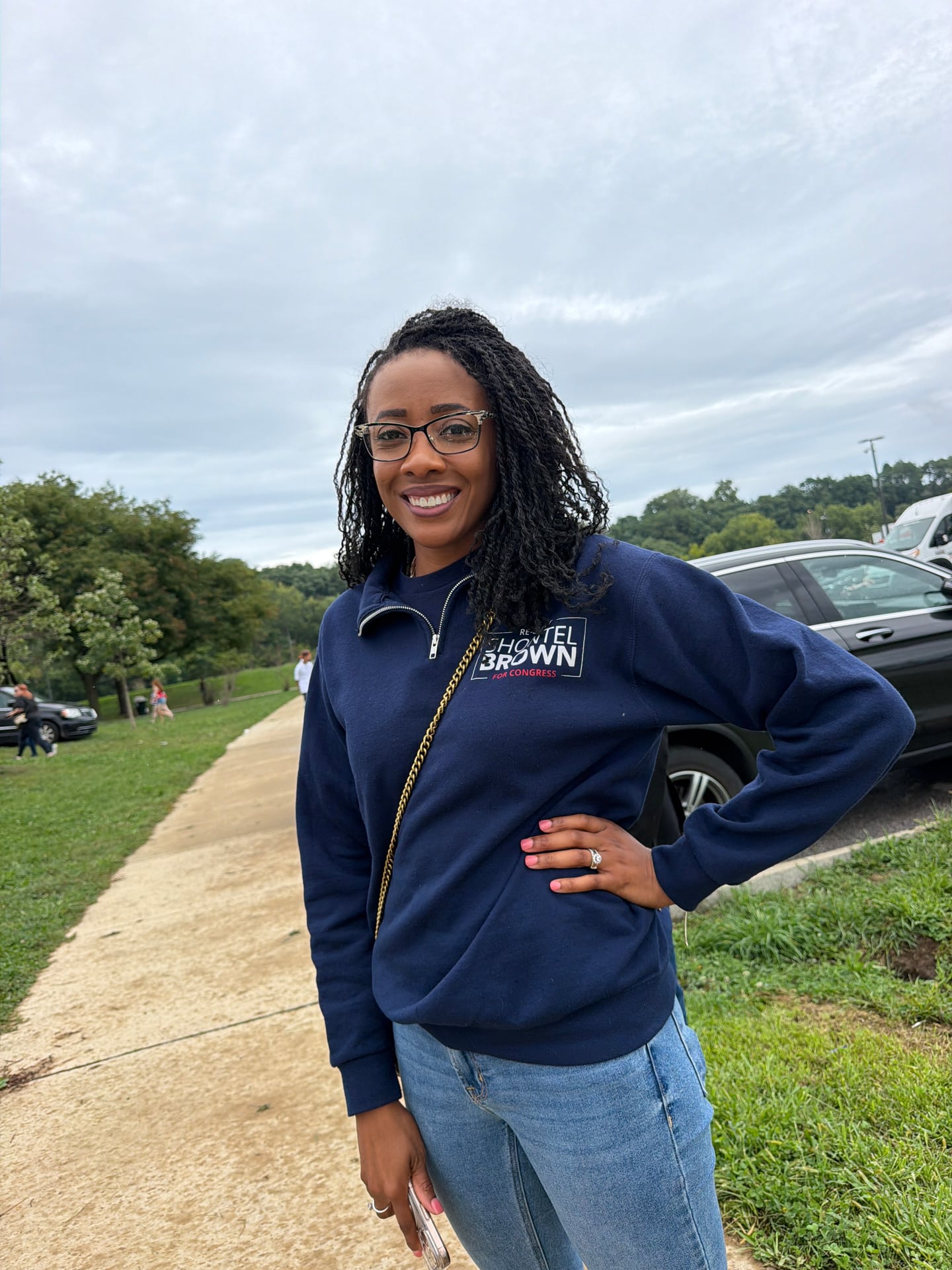 A smiling person in glasses and a navy sweatshirt posing beside a park path.
