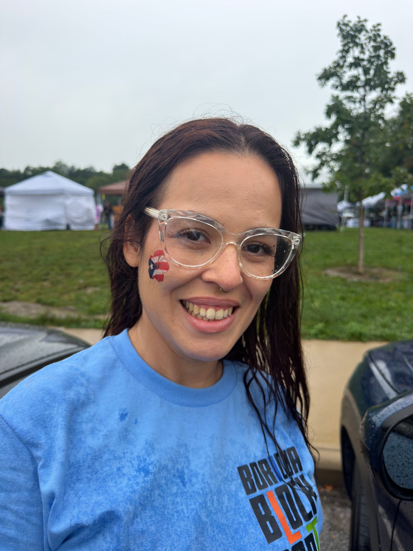A smiling person in a light-blue block party shirt with a Puerto Rican flag design painted on one cheek.