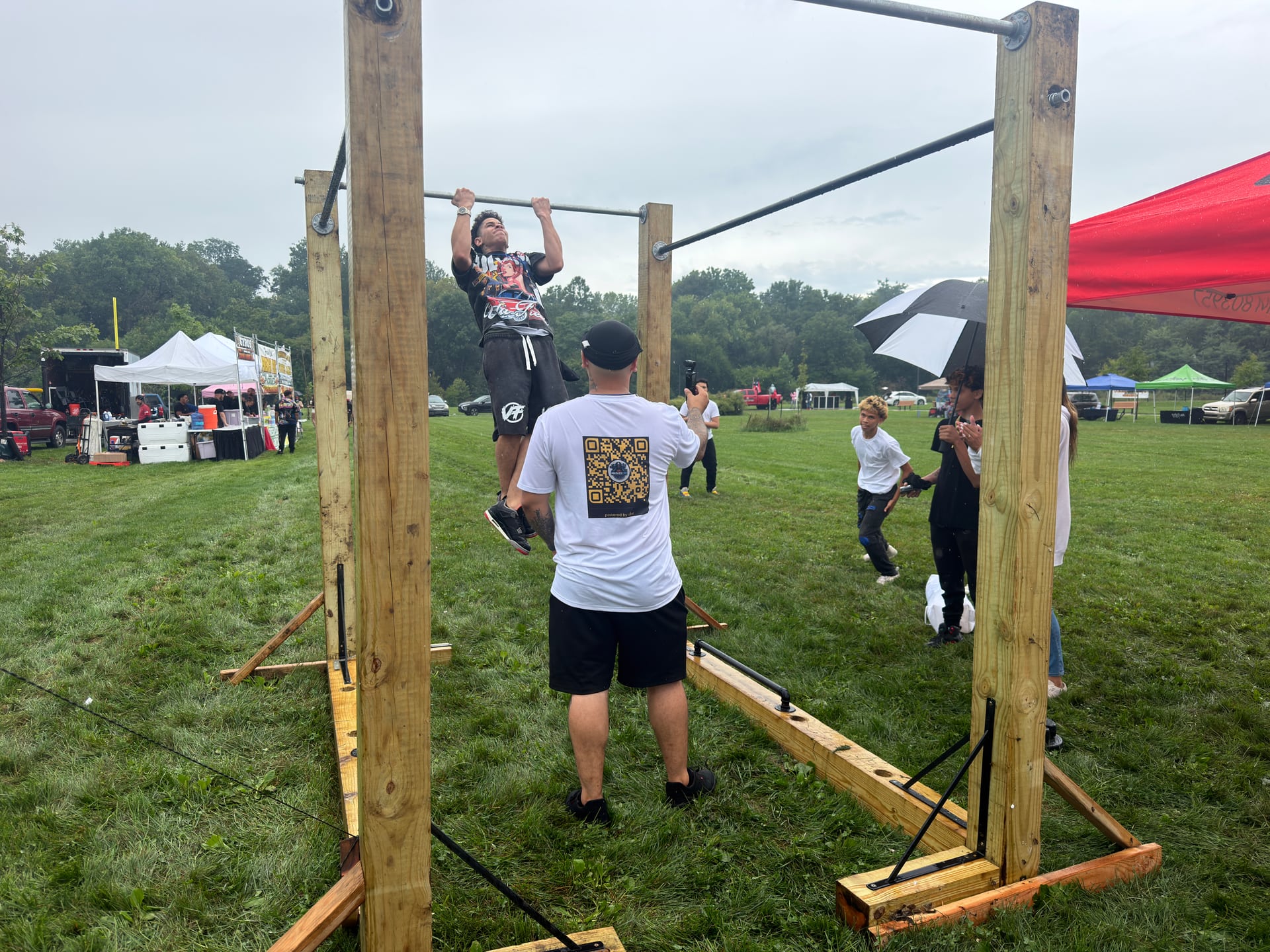 A person performing a pull-up while another records the moment and spectators watch.