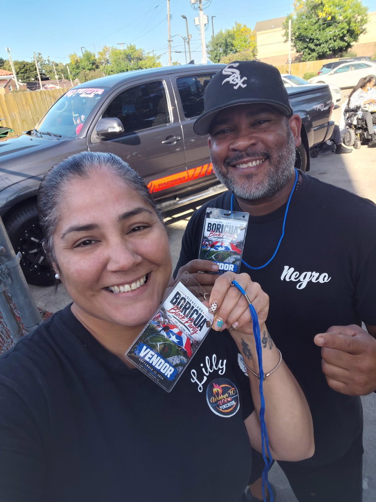 Two smiling people taking a selfie and holding their block party vendor badges.